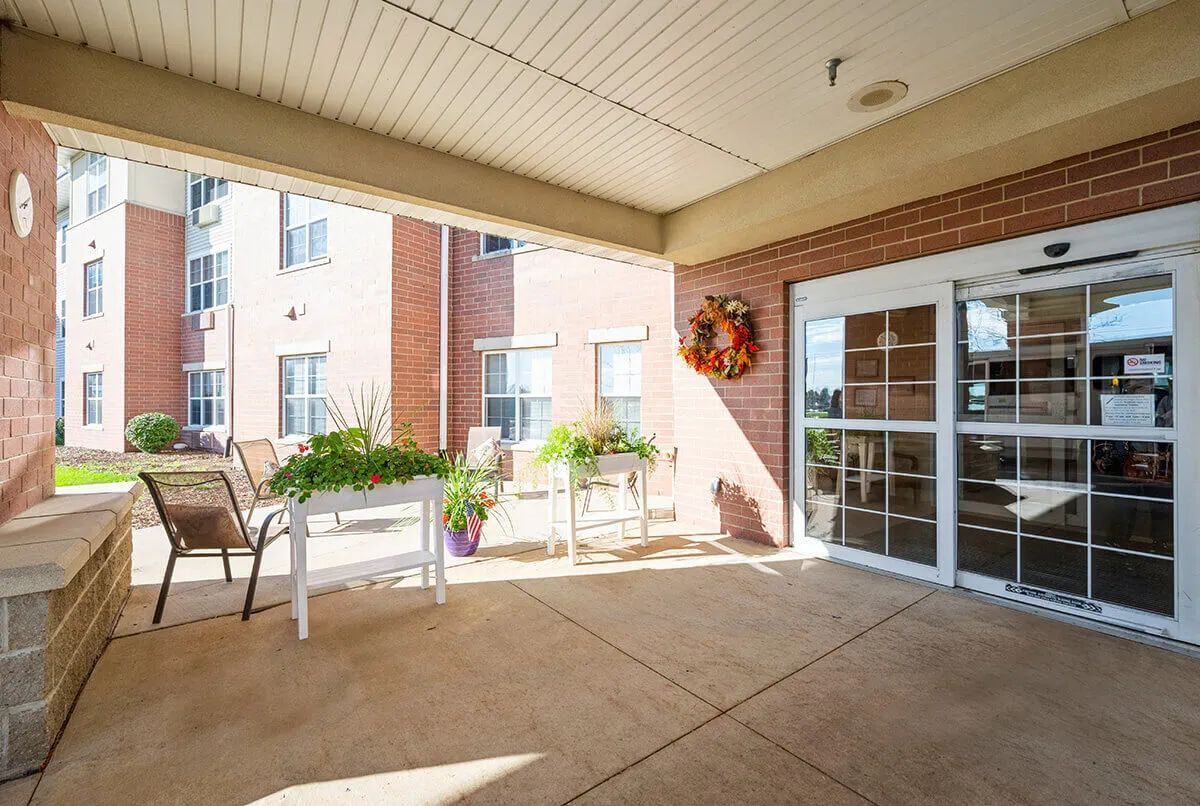 A welcoming porch area with chairs, tables, and potted plants at the entrance of a building.