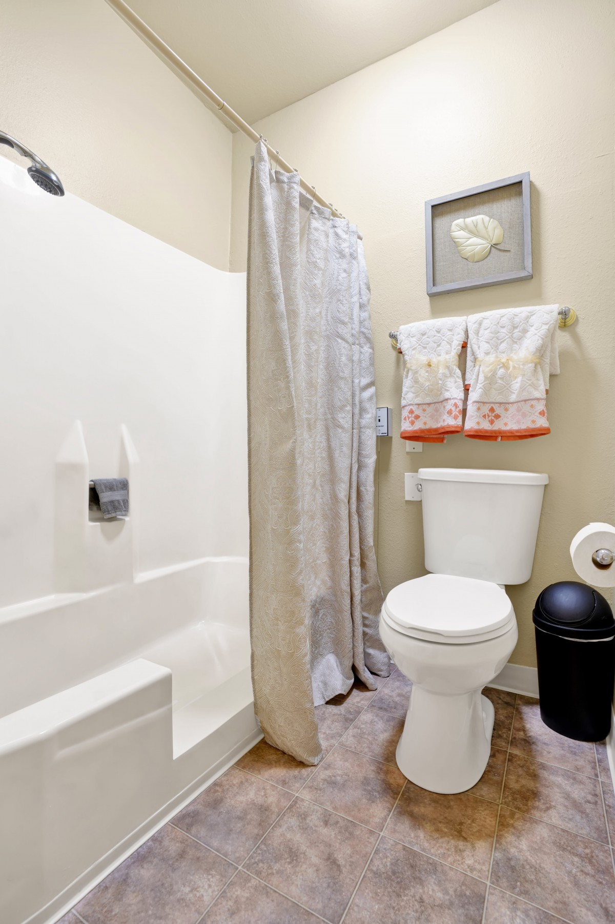 A small bathroom featuring a toilet, shower, and towels neatly hung above.