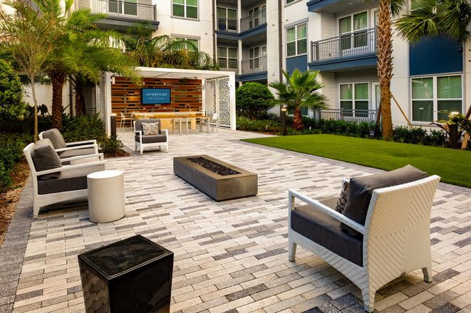 A modern outdoor patio area with comfortable seating and a television, set against the backdrop of an apartment complex.