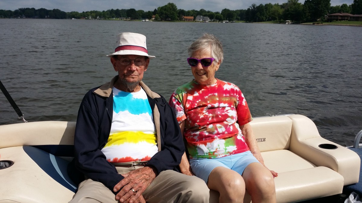 An elderly couple enjoying a boat ride on a sunny day, wearing colorful tie-dye shirts.