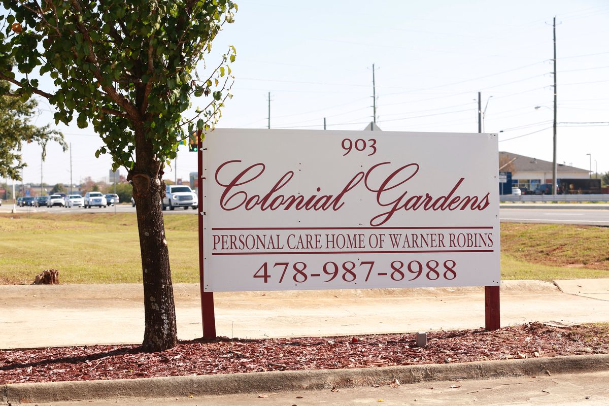 A sign for Colonial Gardens, a personal care home, displaying its address and contact number.