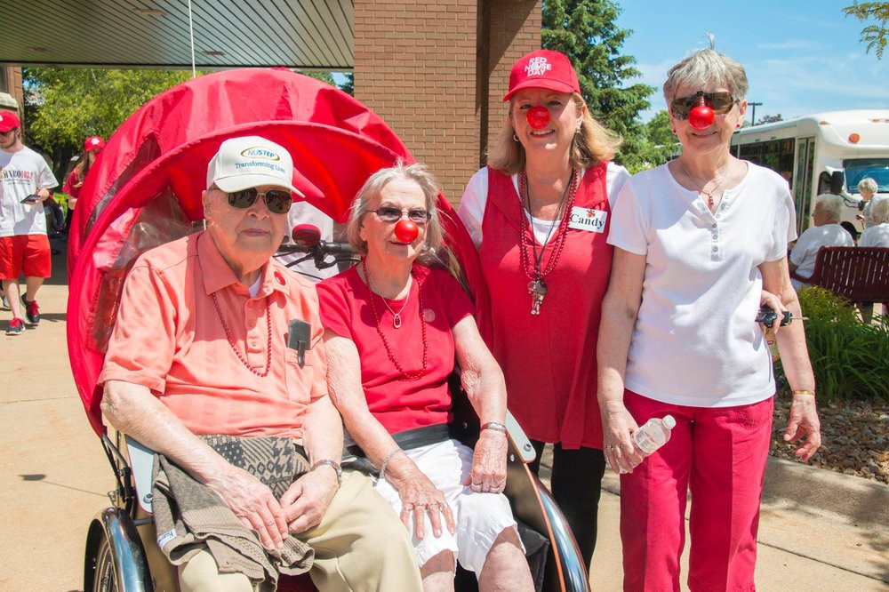 A group of people, some wearing red noses and red clothing, pose together outdoors, possibly during a charity event.