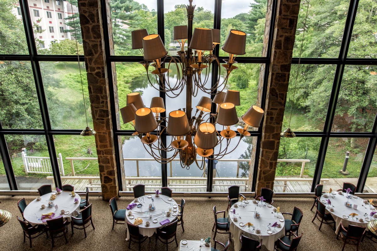 A beautifully set banquet hall showcasing a grand chandelier with large windows offering a view of lush greenery.