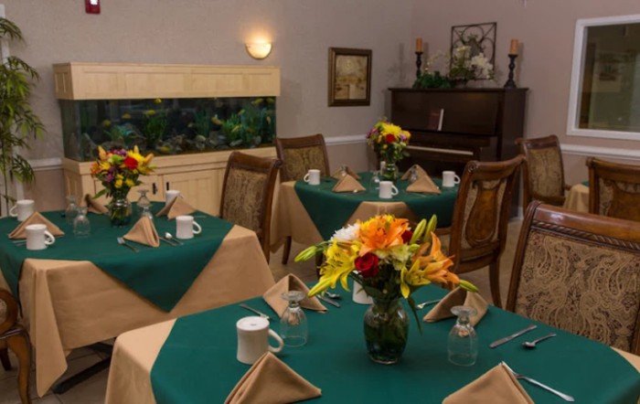 A cozy dining room with elegantly set tables and a piano in the background.
