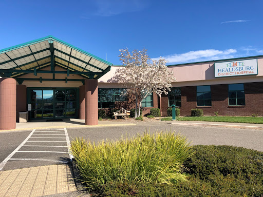 A healthcare facility with a welcoming entrance and blooming tree, set against a clear blue sky.