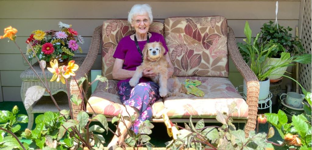 An elderly woman sitting on a garden bench holding her dog.