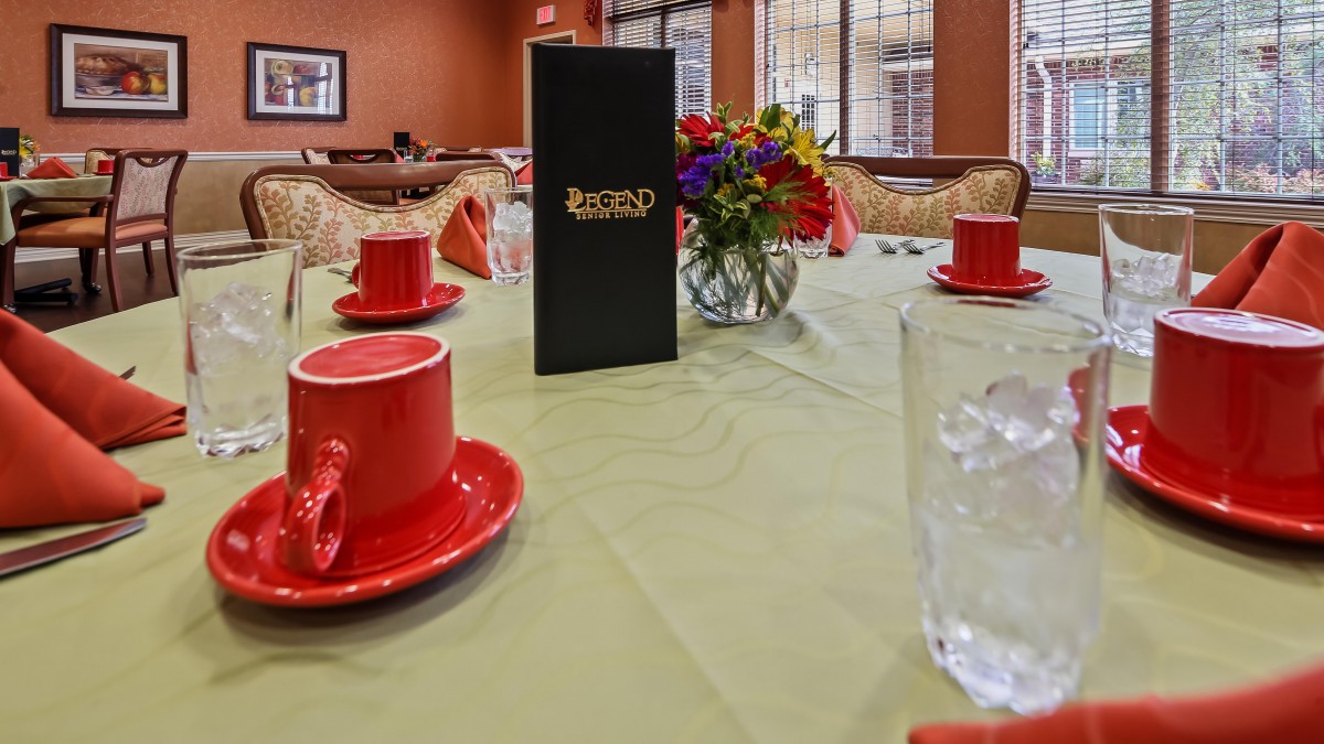 A neatly set dining table with red cups and a menu, accented by a colorful flower arrangement.