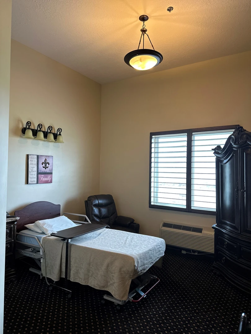 A hospital room with a single bed, recliner chair, and wooden cabinet.