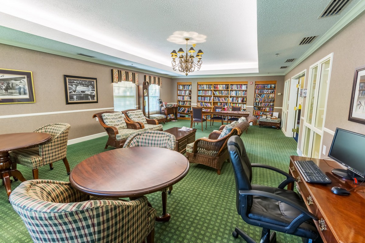A cozy library room with armchairs, tables, and bookshelves.