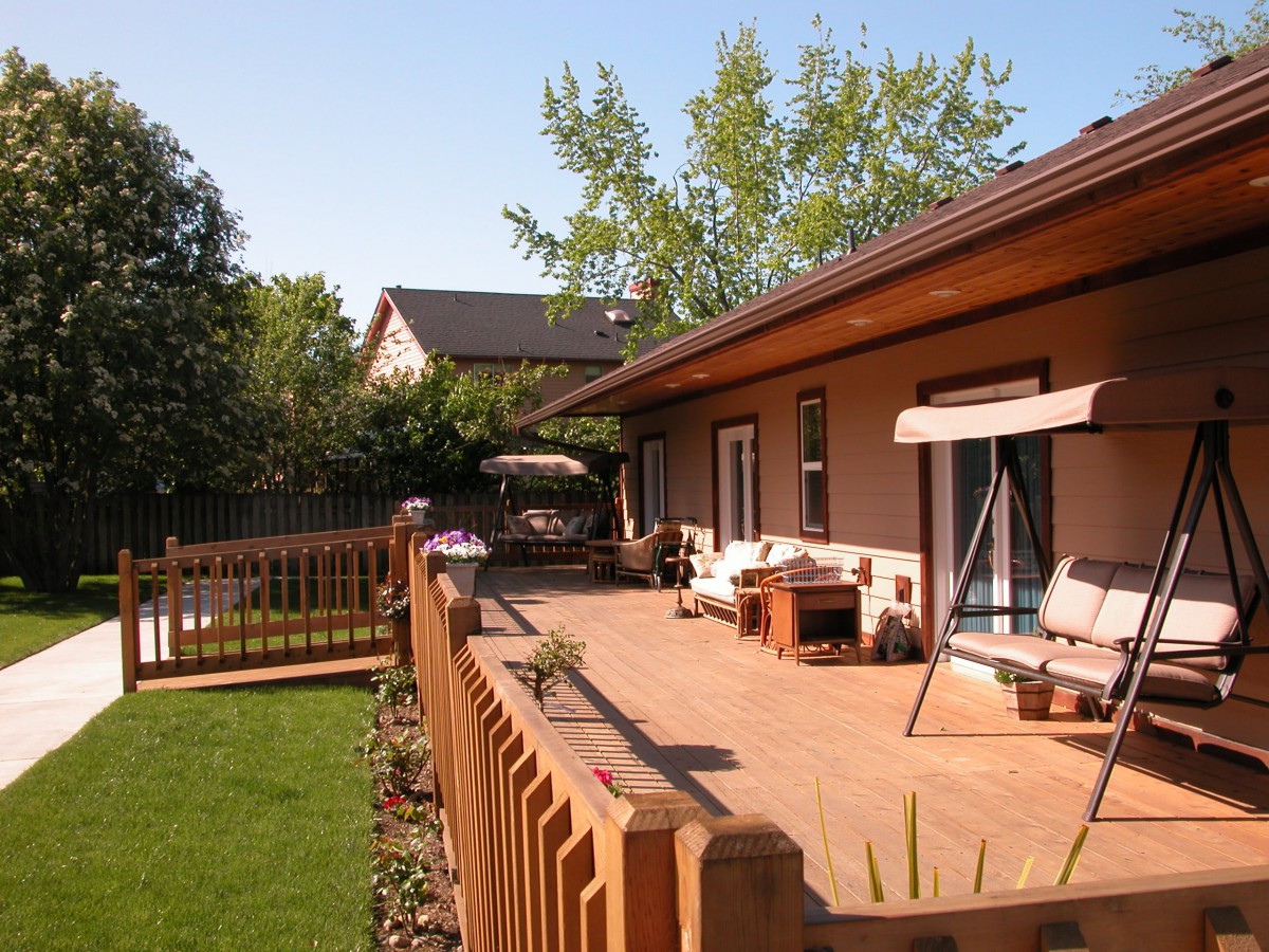 A cozy backyard patio with wooden decking and outdoor furniture, surrounded by a garden and fence.
