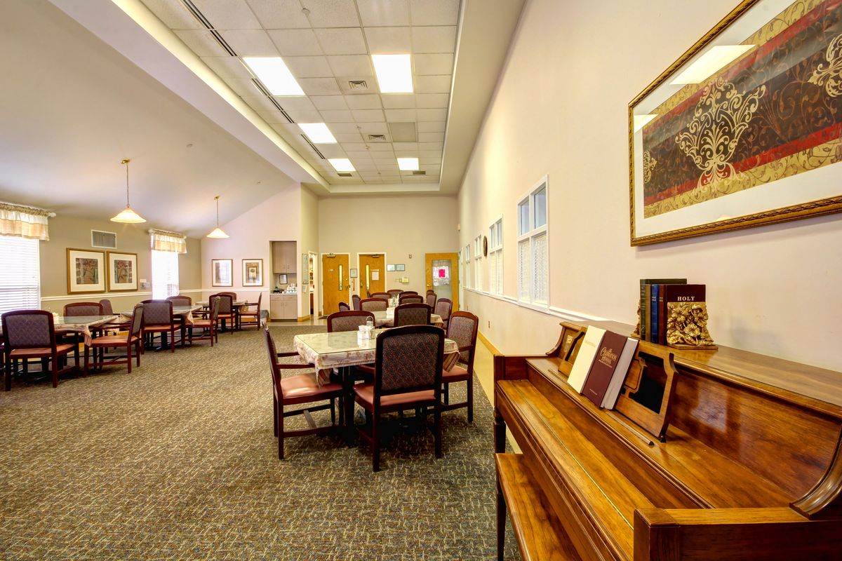 A spacious and well-lit room featuring a dining area with tables, chairs, a piano, and artwork on the walls.