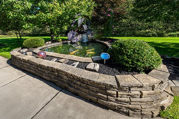 A serene garden pond enclosed by a stone wall and lush greenery.