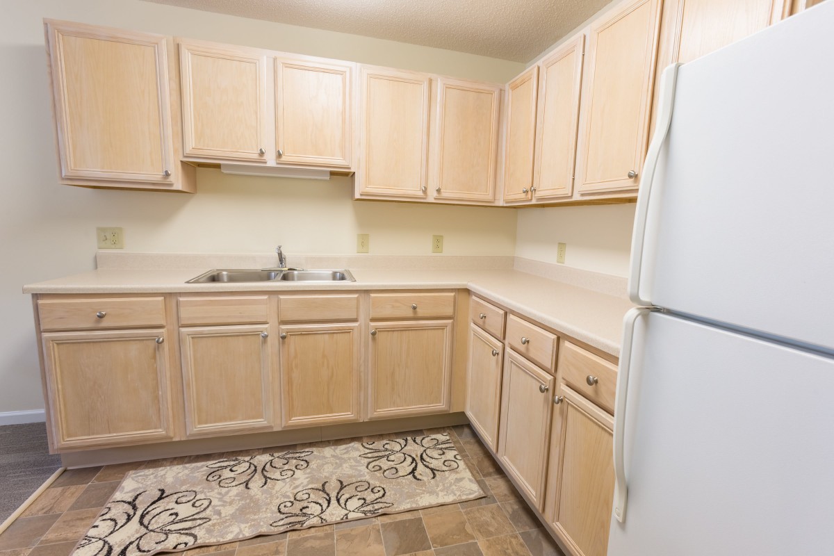 A clean and compact kitchen with light wood cabinets, a white refrigerator, and patterned flooring.