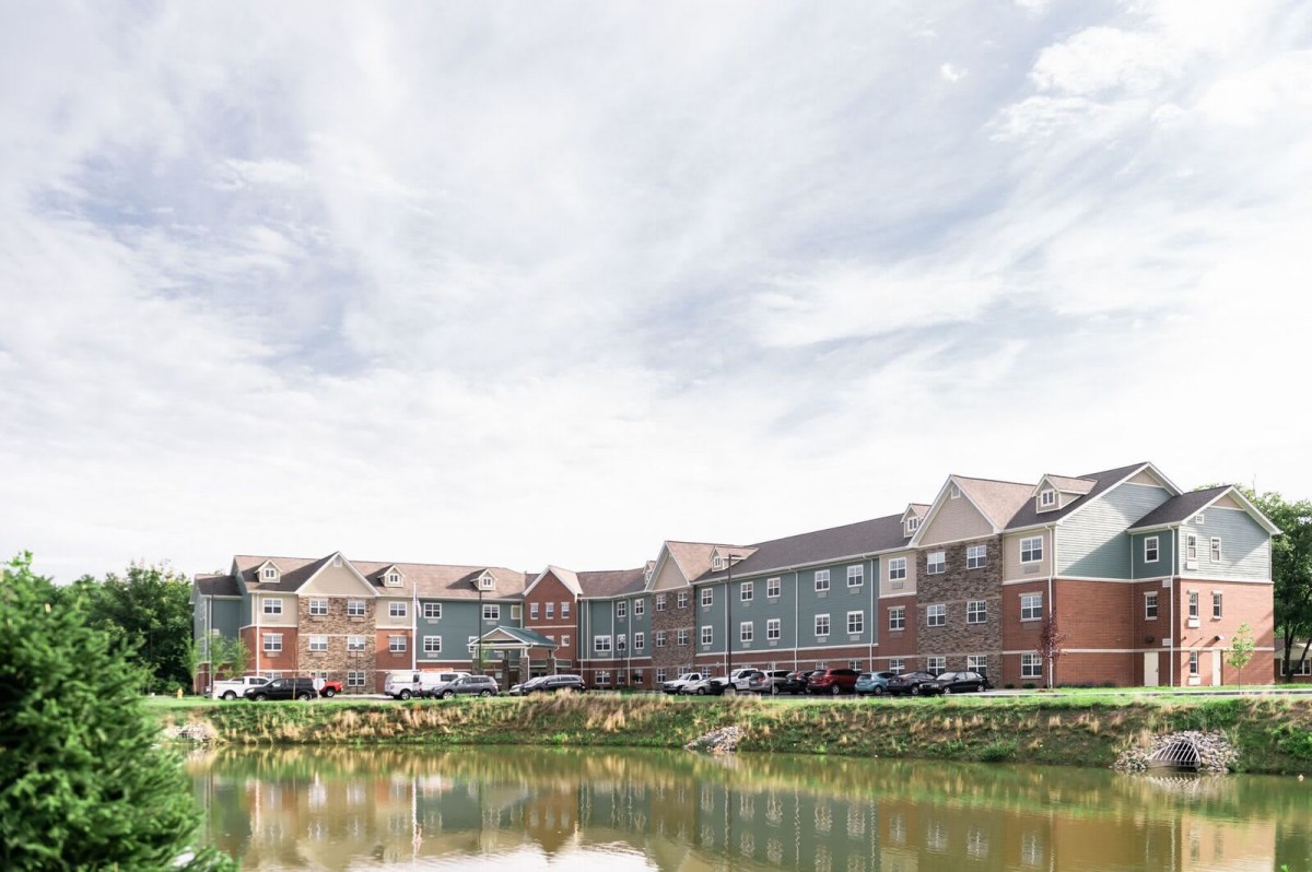A scenic view of a residential area with colorful buildings next to a lake, under a cloudy sky.