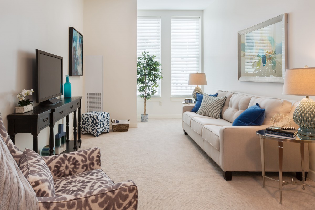 A cozy living room with modern decor, featuring a beige couch, television, and large windows.