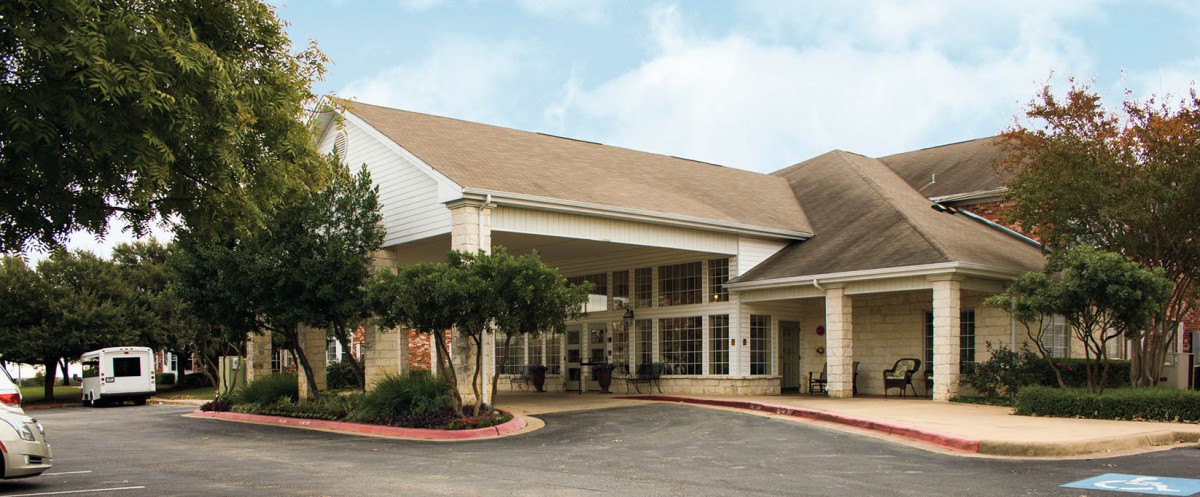The image shows a building with a covered entrance and landscaped surroundings.