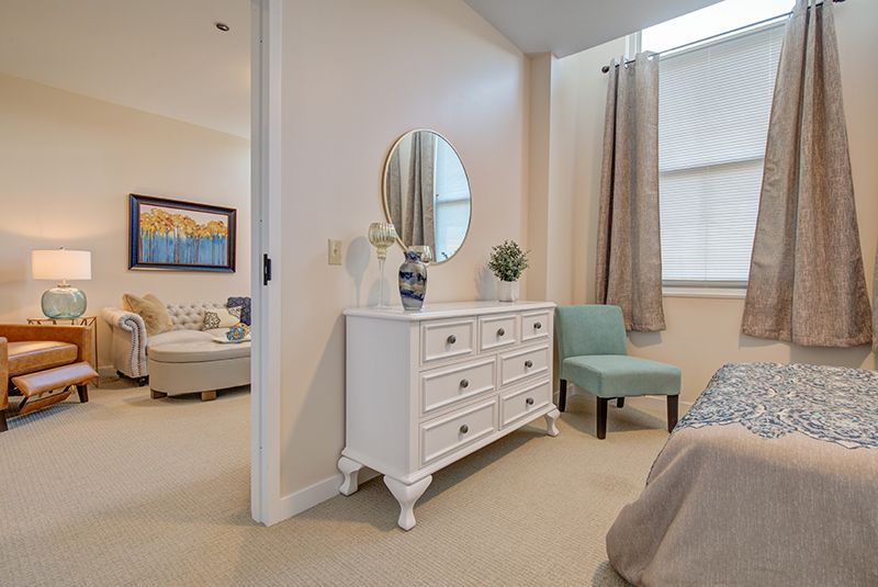 A modern bedroom with a white dresser and circular mirror, featuring elegant decor and neutral tones.