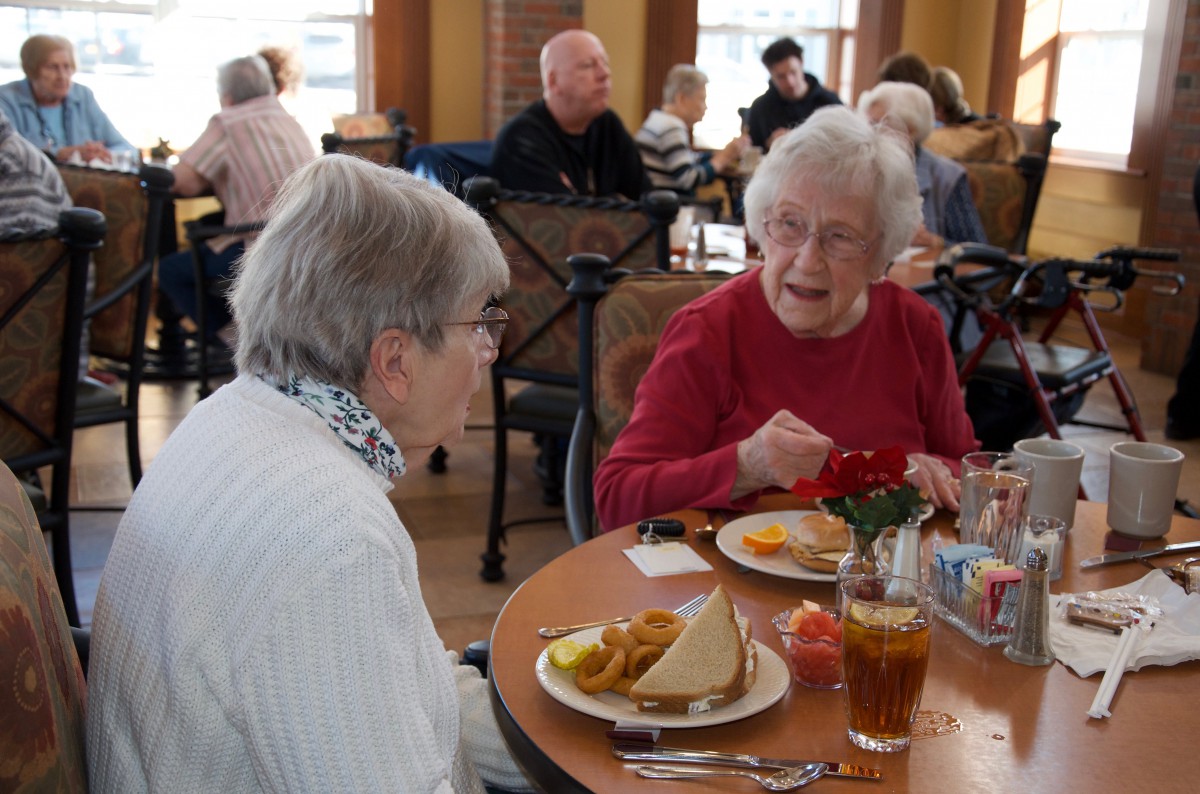 Two elderly women enjoying a meal and conversation in a restaurant setting.