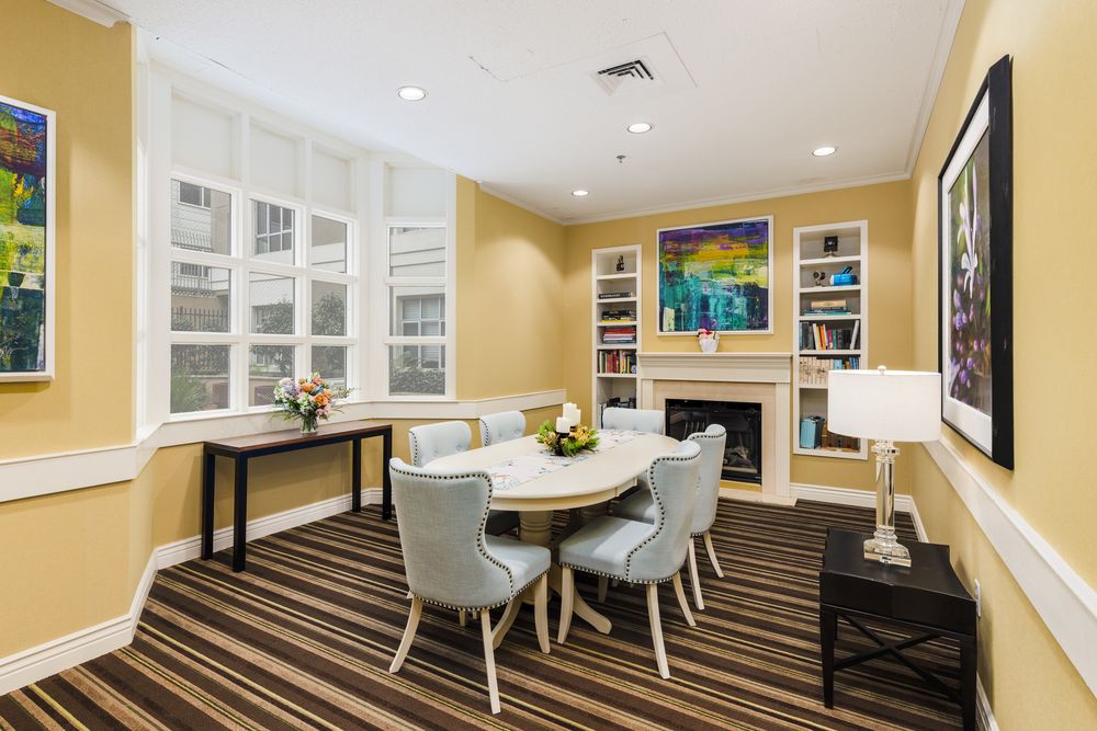 A cozy living room featuring a round table with chairs, bookshelves, and a fireplace, complemented by artwork on the wall.