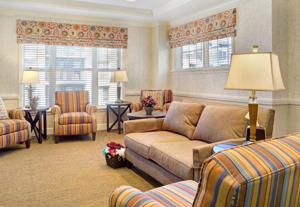 A cozy living room with a sofa, armchairs, and soft lighting complemented by patterned window treatments.