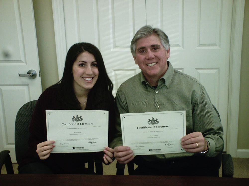 Two people proudly holding certificates indoors.