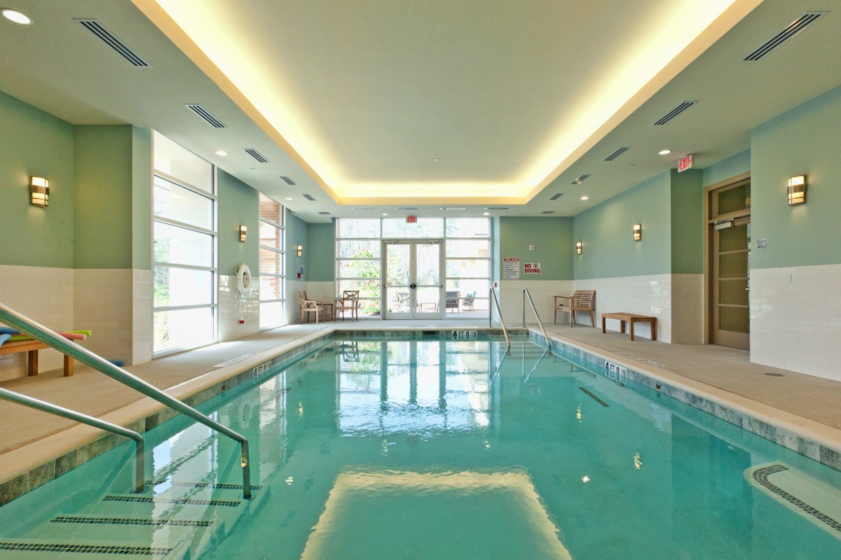A modern indoor swimming pool with natural lighting and a relaxation area.