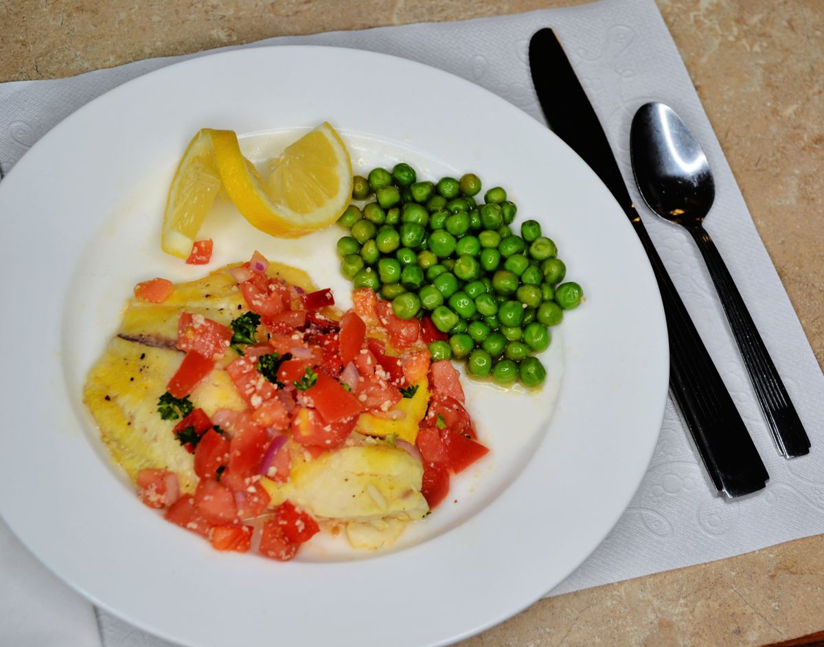 A healthy meal featuring fish with tomatoes and herbs, served with peas and lemon wedges.