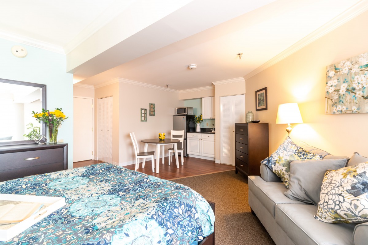 A cozy studio apartment featuring a living area, bed, and kitchenette.