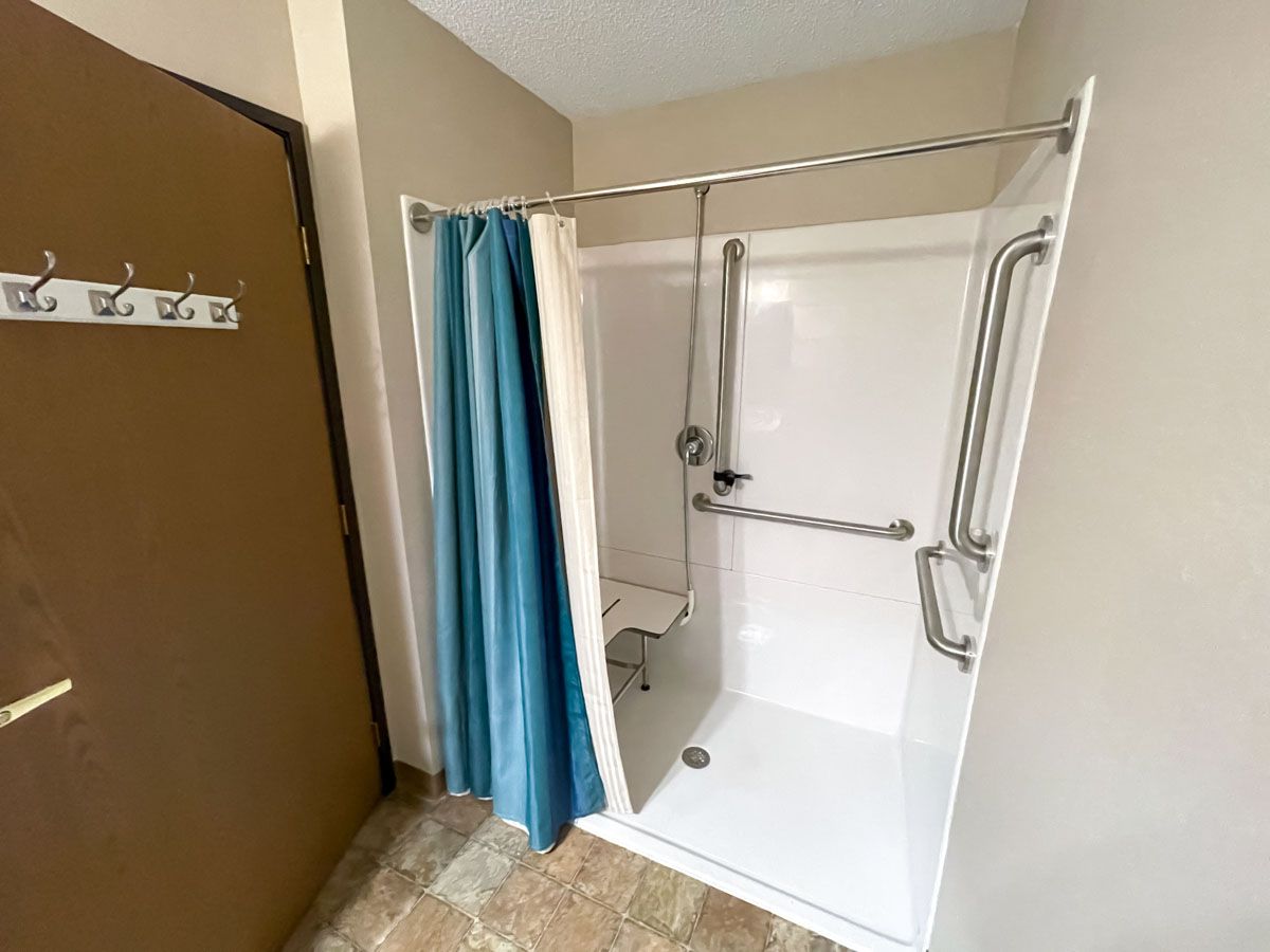 An accessible bathroom shower with safety grab bars and a curtain.