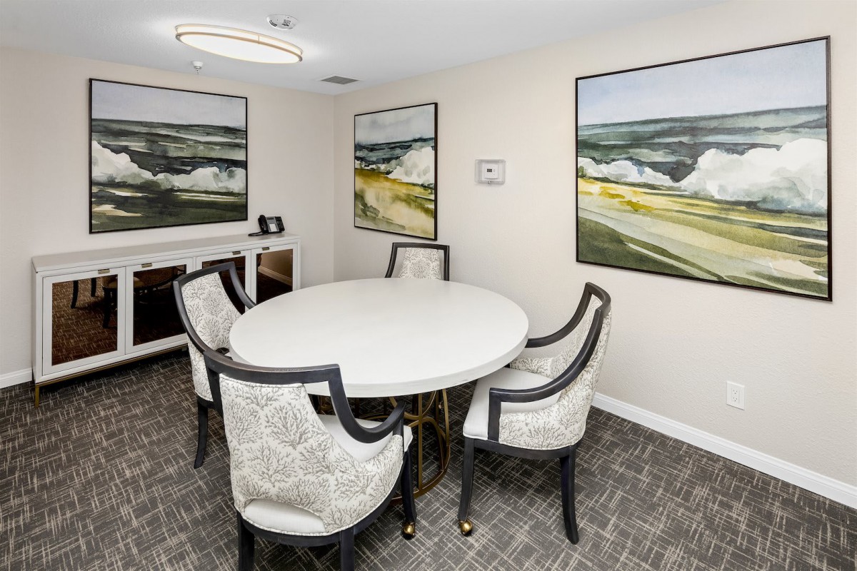 A small, elegantly furnished meeting room with a round table and four chairs, adorned with landscape paintings on the walls.