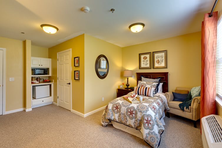 A cozy bedroom with a single bed, kitchenette, and warm yellow walls.