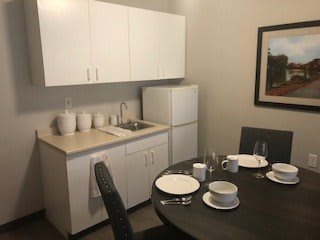 A small kitchen with a dining area, featuring white cabinets, a refrigerator, and a neatly set table.