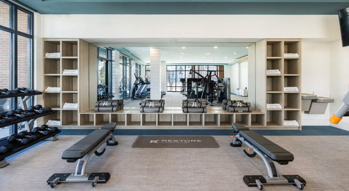 A modern gym equipped with weights, benches, and exercise machines in a spacious, mirrored setting.