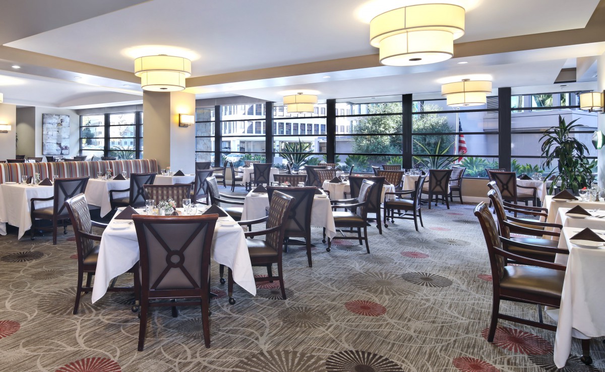 An elegant dining area with neatly arranged tables and chairs, featuring large windows and soft lighting.