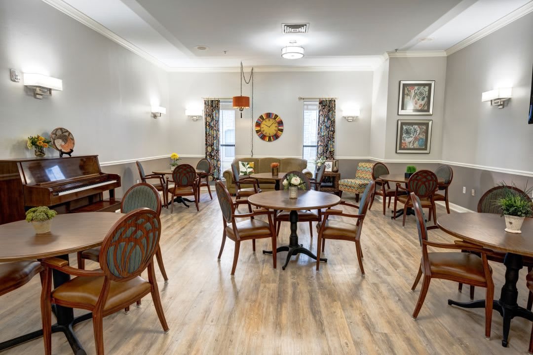 A spacious and elegantly decorated dining area with wooden tables and chairs, featuring a piano and framed art on the walls.