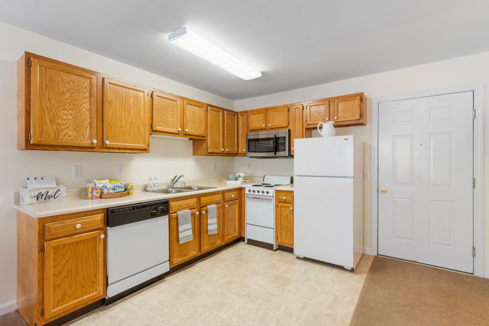 A spacious kitchen with wooden cabinets and white appliances, including a refrigerator, stove, microwave, and dishwasher.