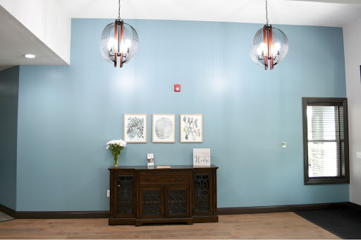 A stylish interior featuring a wooden cabinet, decorative wall art, and contemporary lighting against a soothing blue backdrop.