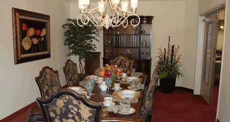 An elegantly set dining room table with a chandelier overhead and floral arrangements as centerpiece.