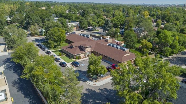 Aerial view of a suburban building surrounded by trees and a parking lot.