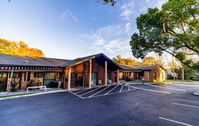 A modern building with a parking lot surrounded by trees under a clear sky.