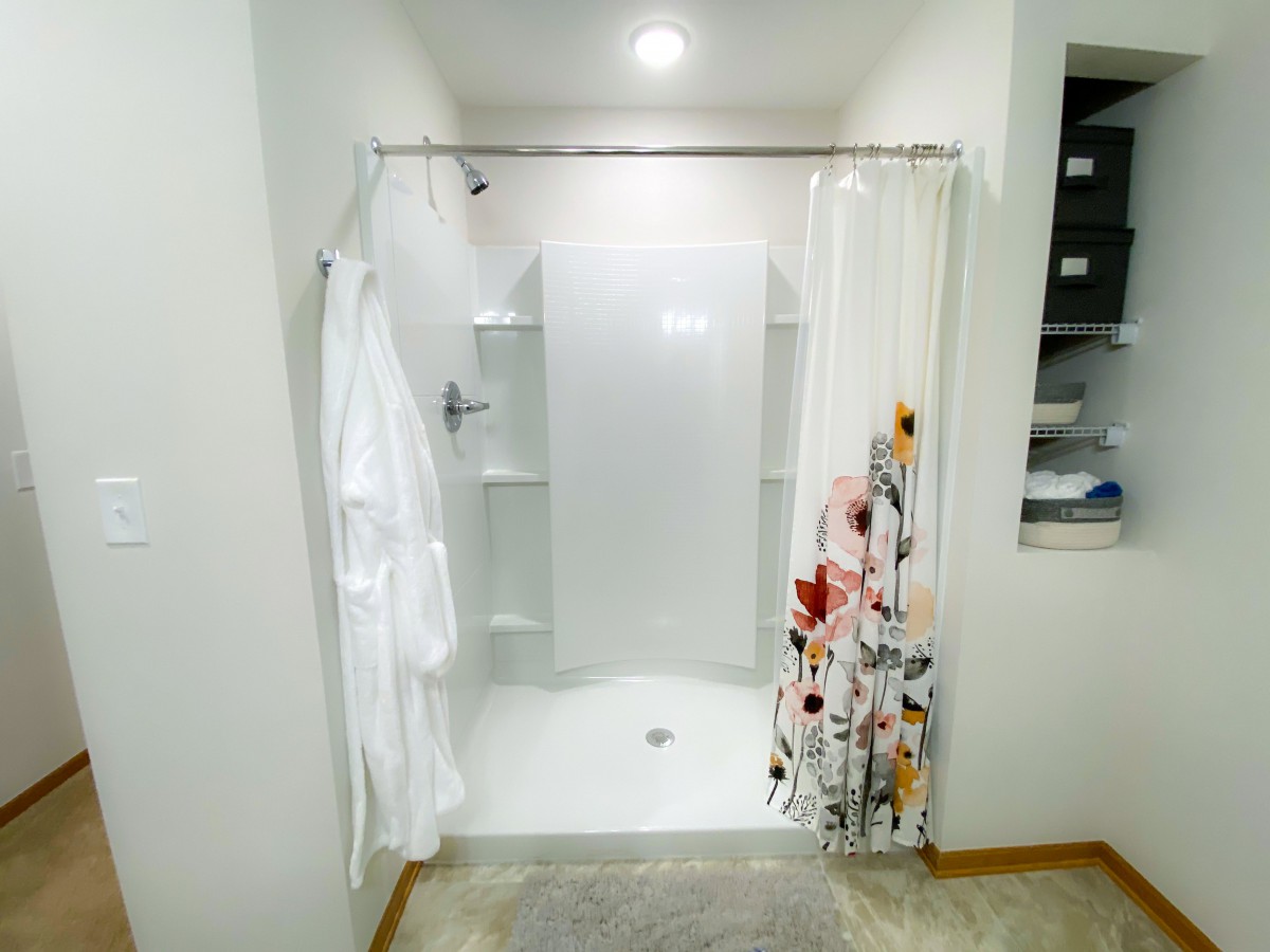 A modern bathroom featuring a walk-in shower with floral and white shower curtains, and a white robe hanging on the side.