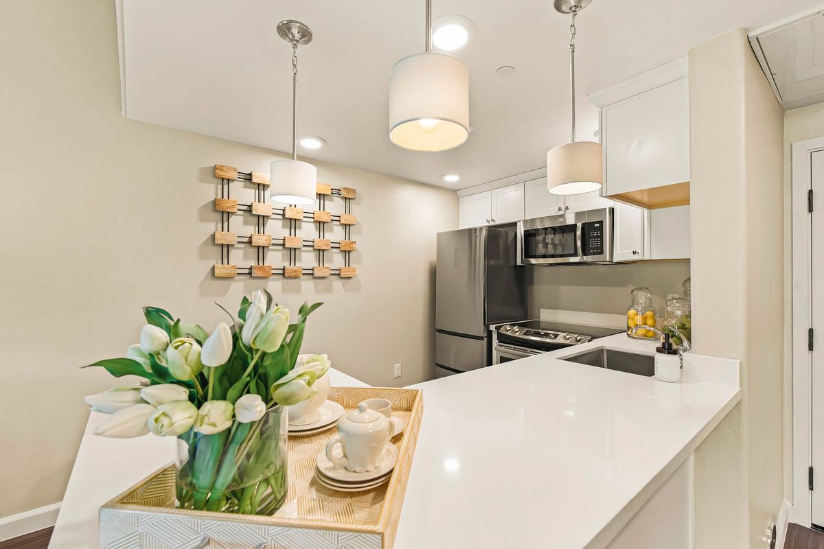 A modern kitchen with white countertops, stainless steel appliances, and elegant pendant lighting.