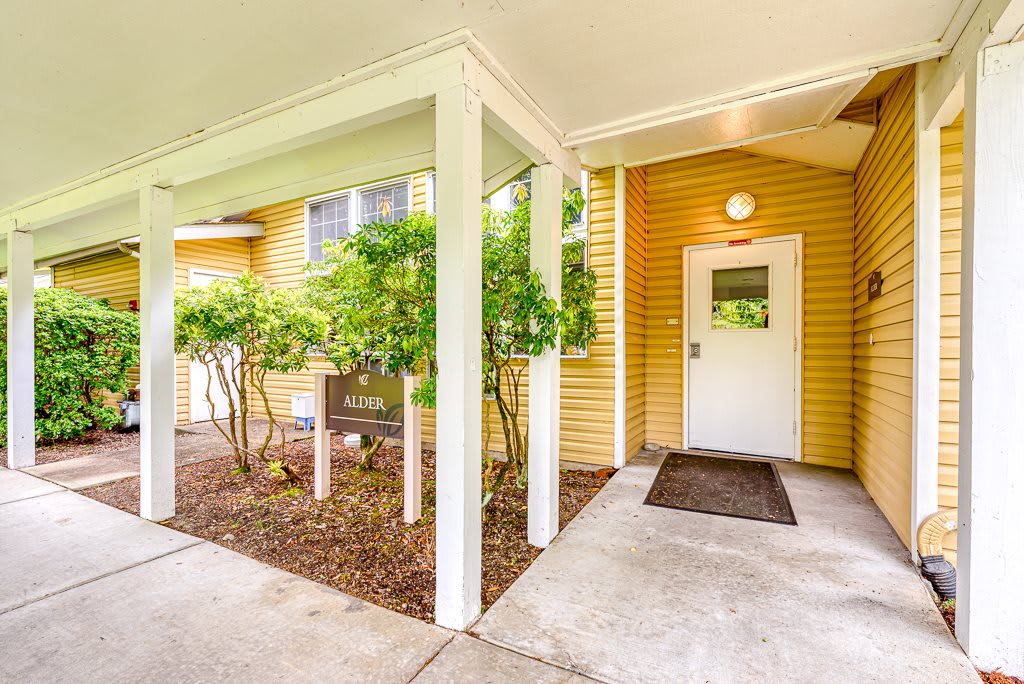 Entrance to a yellow building with a covered walkway and surrounding greenery.