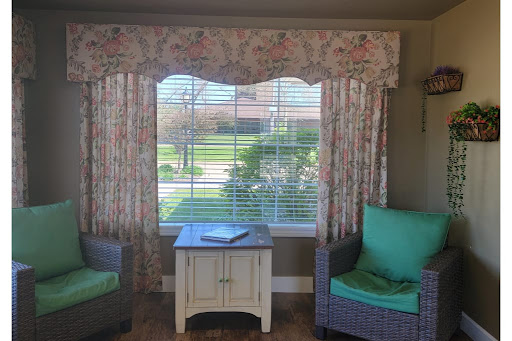 A cozy living space featuring floral curtains, two comfortable chairs, and a small table by the window.