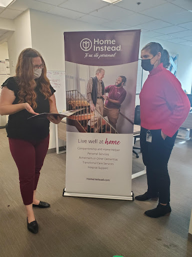 Two individuals interacting in an office setting near a promotional banner.