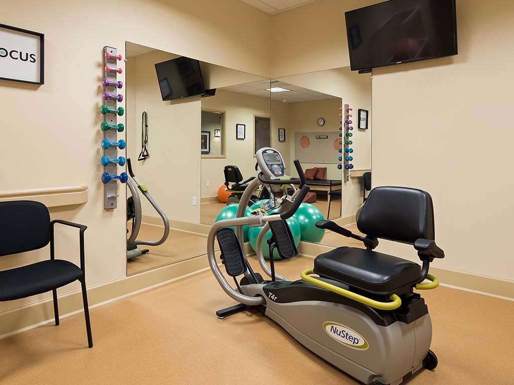 A fitness room featuring a recumbent exercise bike, wall-mounted weights, and a television.