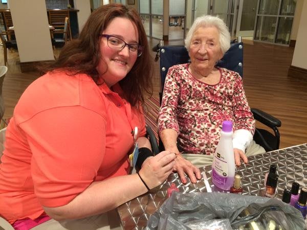 A caregiver is giving a manicure to an older adult, both smiling and enjoying their interaction.