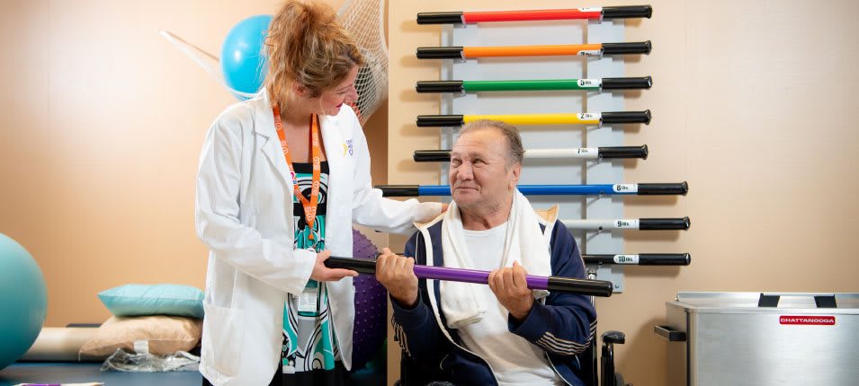 A healthcare professional assists an elderly man during a physical therapy session.