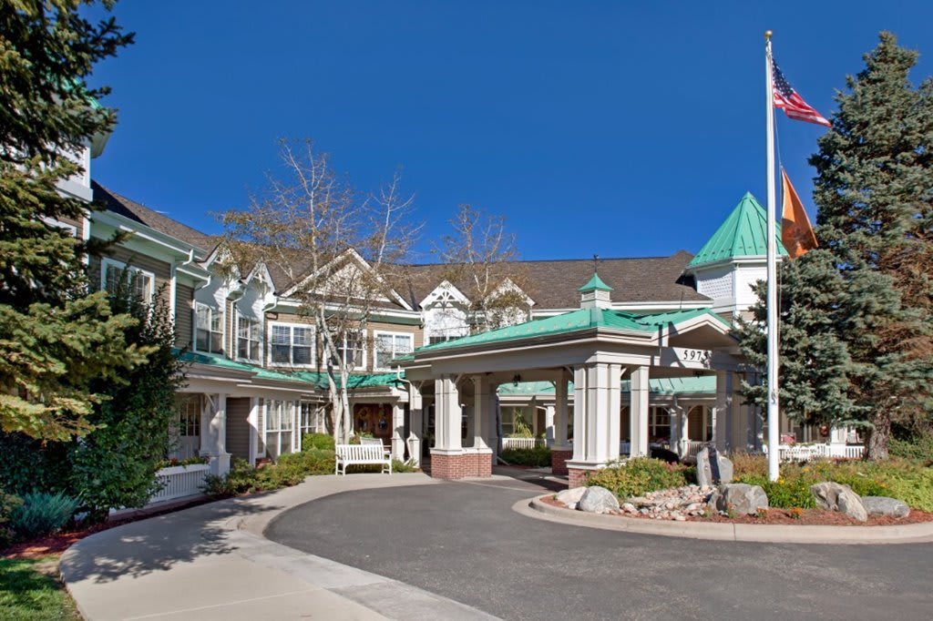 A well-maintained residential building with a covered entrance and driveway, surrounded by greenery.