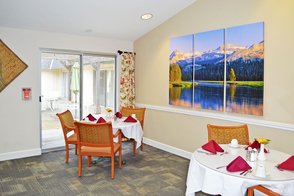 A cozy dining area with neatly set tables and vibrant landscape artwork on the wall.